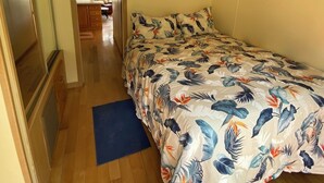 Ein Schlafzimmer mit Bett, Holzboden, Deckenventilator und Blick in einen anderen Raum.
