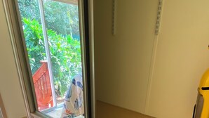 Ein kompakter Raum mit einer Schiebetür zu einem Garten, einem kleinen Holztisch und einem gelben Reinigungswerkzeug.