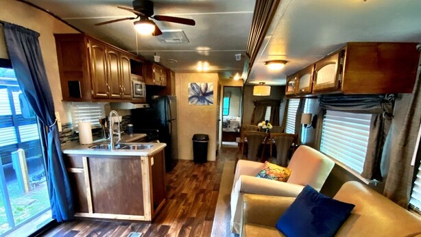 A compact RV interior with a kitchenette, a dining area, and a living space with a sofa and a ceiling fan.