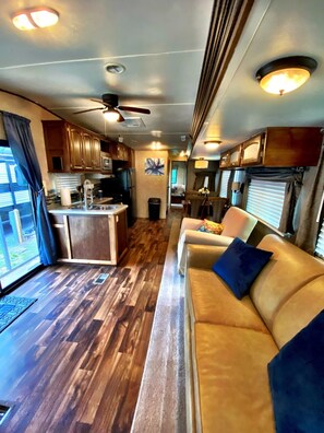 A compact RV interior with a kitchenette, a dining area, and a living space with a sofa and a ceiling fan. - Nice 40’ RV with all modern conveniences, (full kitchen, bathroom, separate bedroom),  in private Resort/campground, pool, hot tub, sauna, clubhouse available to all guests. (Pace)