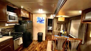 A compact RV kitchen with a microwave, stove, refrigerator, and a dining area with chairs and a table.