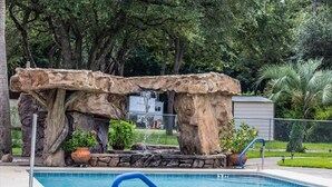A pool area with a natural rock feature, a small waterfall, and potted plants.