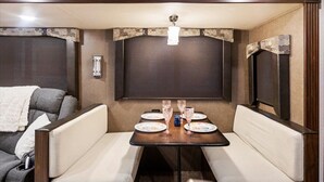 A compact RV interior with a dining area, two sofas, and a small table set for four.