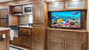 A kitchen with wooden cabinetry, a microwave, and a large flat-screen TV displaying an underwater scene.