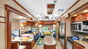 Interior compacto de una caravana con kitchenette, comedor y sala de estar con sofá y televisor.