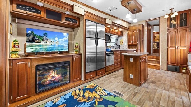 Una cocina amplia con armarios de madera, un refrigerador grande y un televisor de pantalla plana sobre la chimenea.