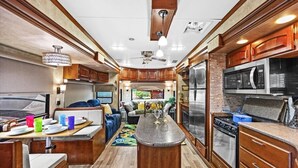 Cocina de autocaravana bien equipada con armarios de madera, una isla central y electrodomésticos modernos.