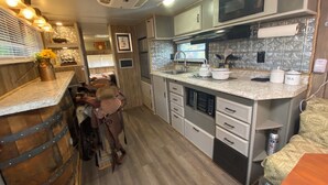 A compact kitchen with a microwave, stove, and sink. There is a bar area with stools and a decorative vase.