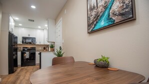 A modern kitchen with white cabinets, a black refrigerator, and a microwave. There is a dining table with chairs and a potted plant. - Charming 1-Bedroom with AC, private yard, & full kitchen (Yuma)