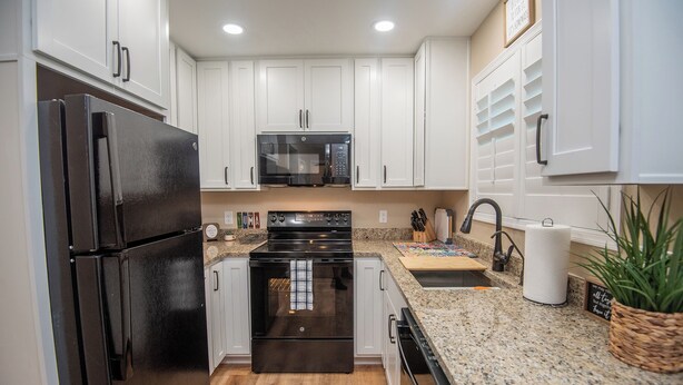 A modern kitchen with white cabinets, a black refrigerator, a microwave, and a granite countertop. - Charming 1-Bedroom with AC, private yard, & full kitchen (Yuma)