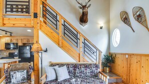 Eine Holztreppe mit einem darüber aufgehängten Hirschkopf, ein gemustertes Sofa und ein Esstisch mit Kerzen.