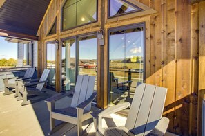 Un espacio al aire libre con techo, con sillas Adirondack y grandes ventanales que ofrecen vistas del paisaje circundante.