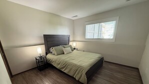 Un dormitorio con una cama, dos mesitas de noche, una ventana y suelo de madera.
