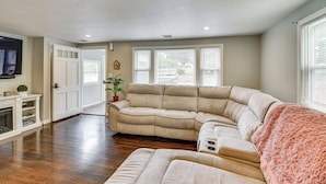 A living room with a sectional sofa, a fireplace, and a large window with blinds. - Stay & Play in Plymouth: Spacious Home w/ Yard (Plymouth)