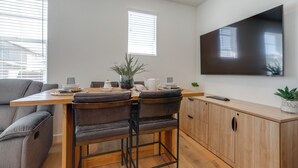Een moderne eetruimte met een houten tafel, twee grijze banken en een aan de muur bevestigde televisie.