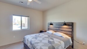 Un dormitorio con una cama, un ventilador de techo, una mesita de noche, una ventana y una lámpara de pared.