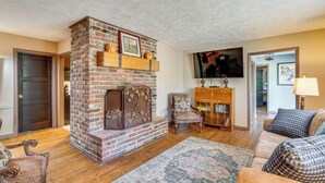 Ein Wohnzimmer mit Kamin, Sofa, Sessel, Bücherregal und Fernseher.
