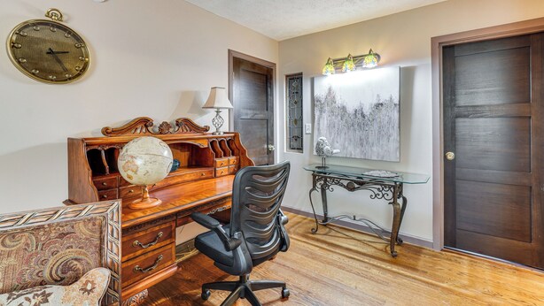 A room with a wooden desk, a globe, a black office chair, a glass table with a lamp, and a painting on the wall.