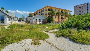 Una propiedad frente a la playa con un edificio grande que tiene varios balcones, una playa de arena y vegetación circundante.