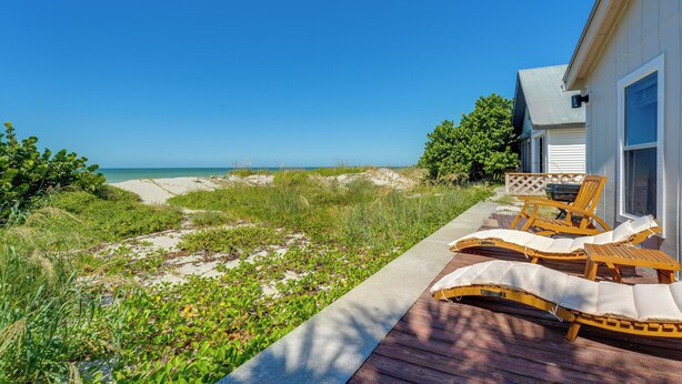Una terraza de madera con sillones de descanso y un sendero que lleva a la playa.