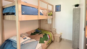 Habitación con literas de madera, una mesita de noche pequeña, una mesita auxiliar y un estante en la pared con una planta.