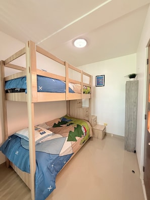 Habitación con literas de madera, una mesita de noche pequeña, una mesita auxiliar y un estante en la pared con una planta.