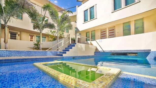 A swimming pool with blue mosaic tiles, a hot tub, and a staircase leading to a balcony.
