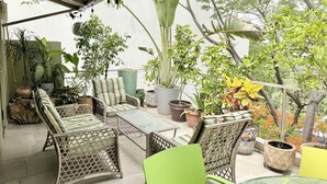 Un espacio al aire libre techado con mobiliario de mimbre, plantas en macetas y vistas al follaje circundante.