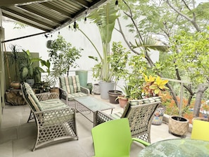 Un espacio al aire libre techado con mobiliario de mimbre, plantas en macetas y vistas al follaje circundante.