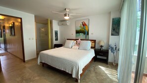 A bedroom with a bed, a nightstand, a lamp, a painting, and a ceiling fan. - Entire Charming condo unit in the heart of Playa Del Carmen (PLAYA DEL CARMEN)