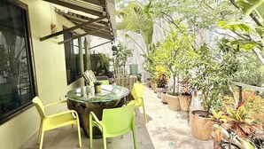 A patio with a round glass table and chairs, surrounded by potted plants and trees.