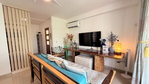 A modern living room with a wooden bench, a TV, a small table with decorative items, and an air conditioning unit.