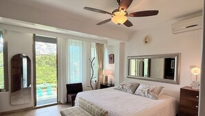 A spacious bedroom with a large bed, a ceiling fan, and a view of the outdoors through a sliding glass door.