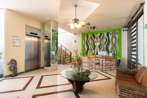 A modern lobby with a glass table, wooden chairs, a staircase, and a green patterned wall. - Entire Charming condo unit in the heart of Playa Del Carmen (PLAYA DEL CARMEN)