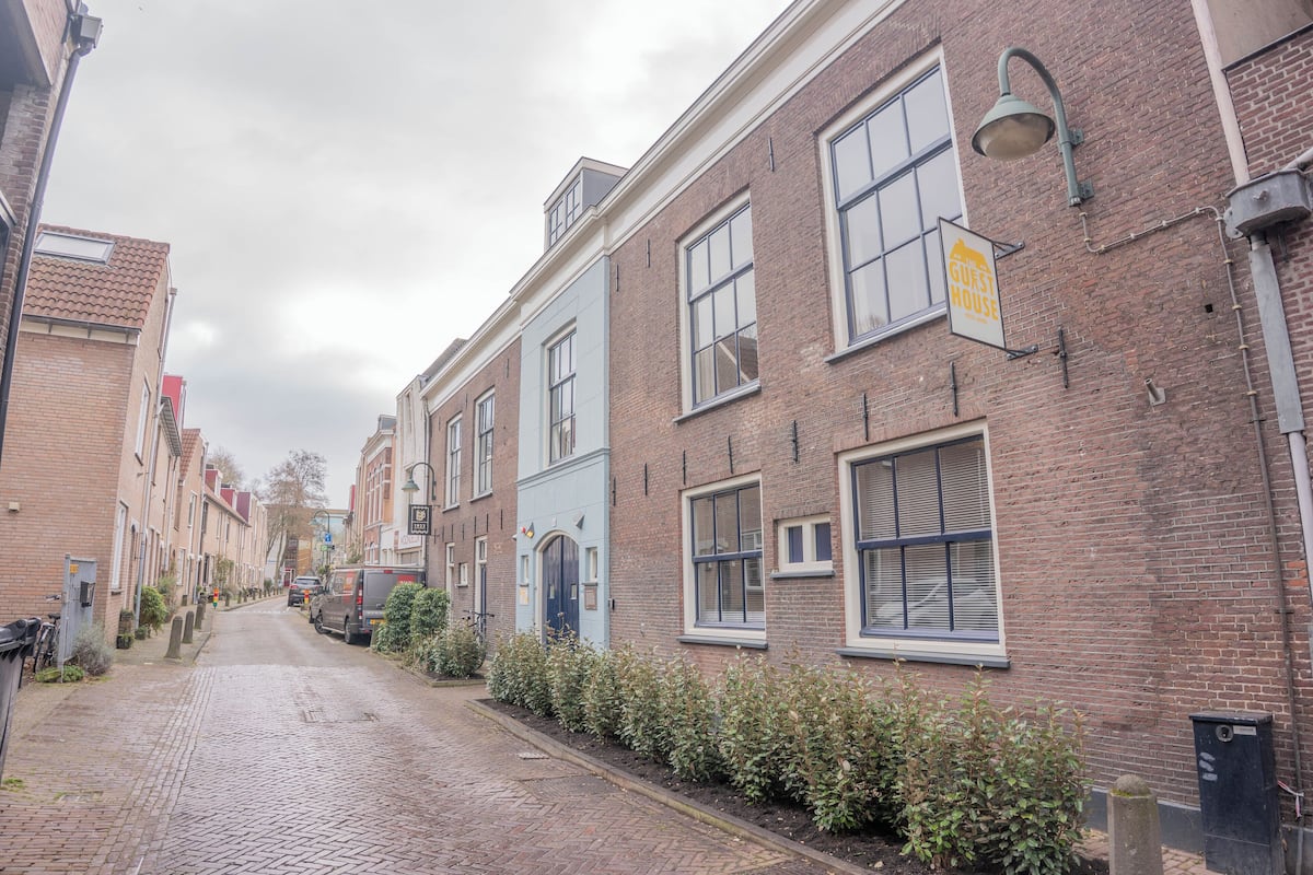 A narrow cobblestone street lined with traditional brick buildings, including a blue building with a sign indicating it is a guest house.