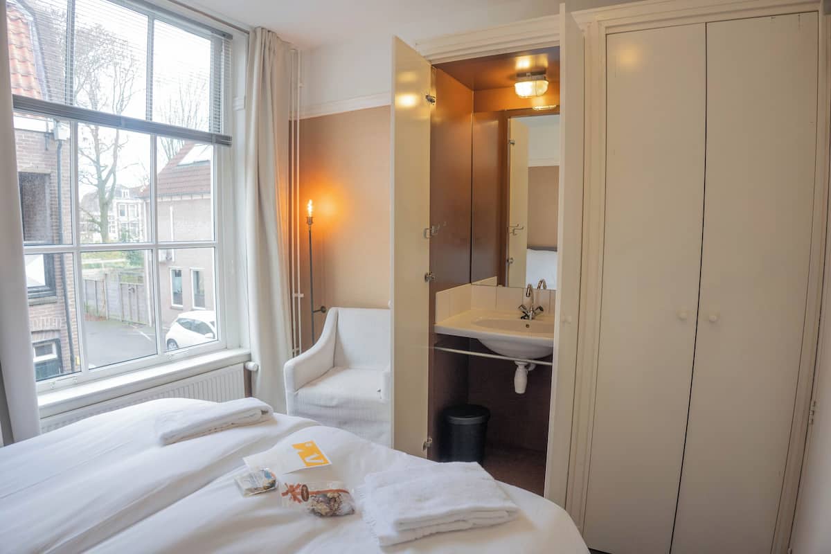 A hotel room with a bed, a chair, a bathroom with a sink, and a window with a view of the street.