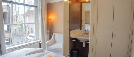 Habitación de hotel con cama, una silla, baño con lavamanos y ventana con vista a la calle.