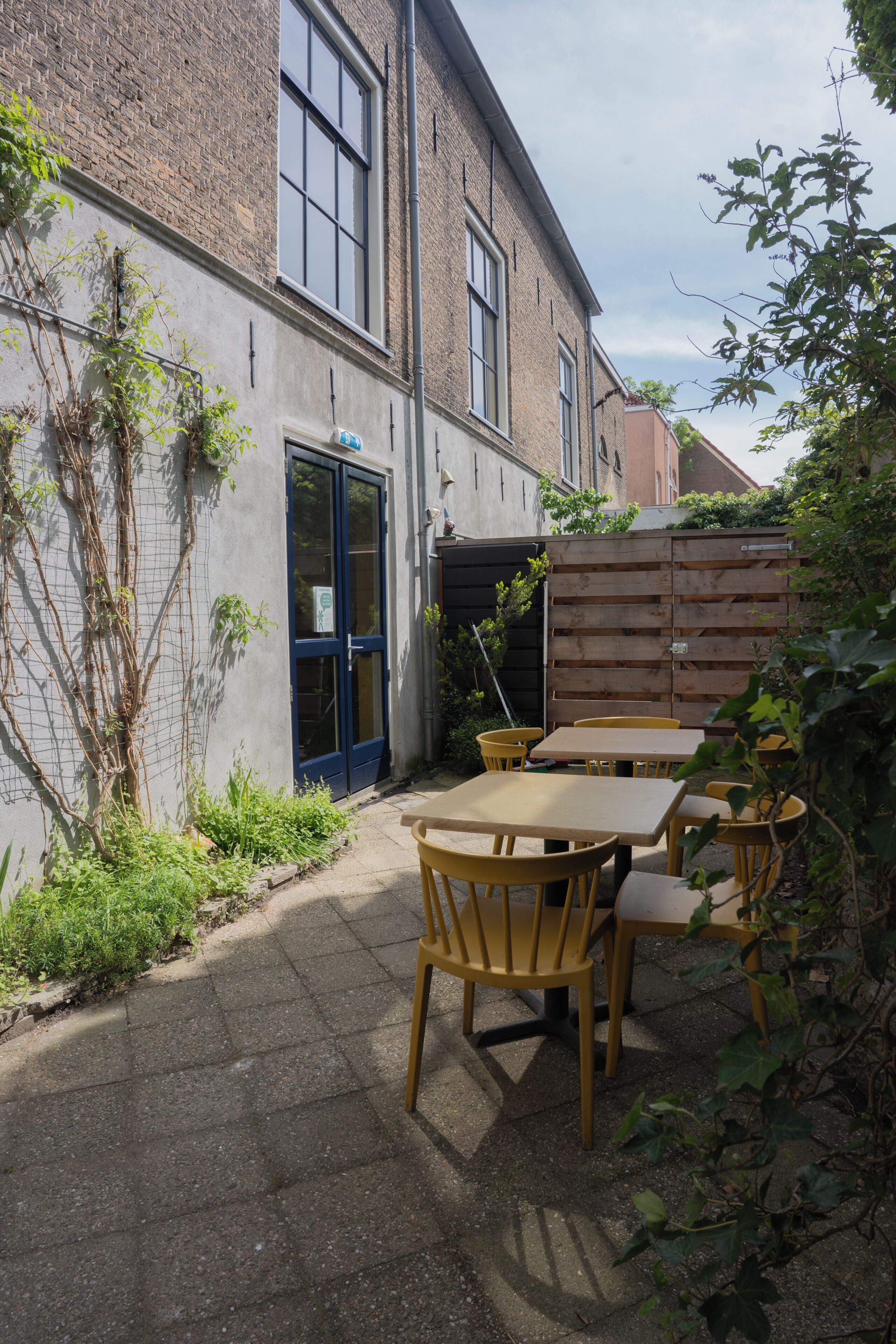 A courtyard with a brick building, a blue door, and wooden tables and chairs.