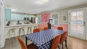 A modern kitchen with teal cabinets, a central island, and a dining area with a patterned tablecloth and orange chairs. - Trendy & Relaxing: Close to Beach ~ Pool ~ Hot Tub (Sarasota)