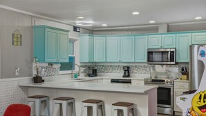 A modern kitchen with teal cabinets, a central island with stools, a microwave, a refrigerator, and a coffee maker. - Trendy & Relaxing: Close to Beach ~ Pool ~ Hot Tub (Sarasota)