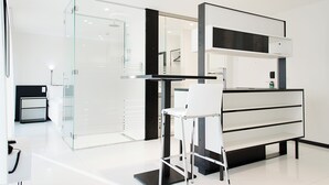 A modern hotel room with a glass shower enclosure, a white desk with a chair, and a black and white console table.