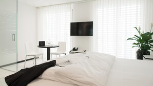 Une chambre d’hôtel moderne équipée d’un lit, d’un bureau, d’une chaise, d’une télévision et d’une plante en pot.