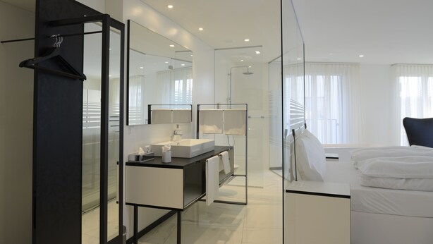 A modern hotel room with a large bed, a bathroom with a glass shower enclosure, and a separate dressing area.
