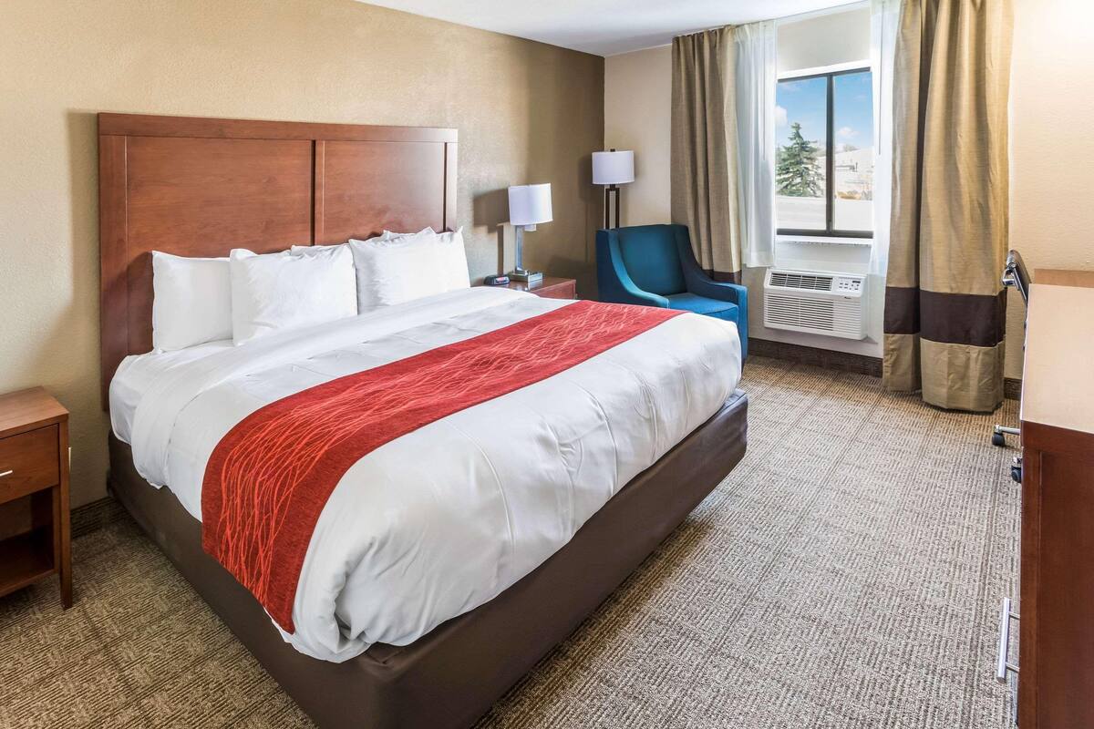 A hotel room with a large bed, a nightstand, a chair, a lamp, and a window with curtains.