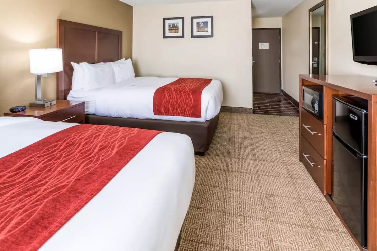 A hotel room with two beds, a desk with a lamp, a TV, and a minibar.
