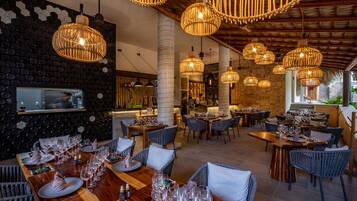 A restaurant with multiple dining areas, wicker pendant lighting, and a stone wall with hexagonal patterns.