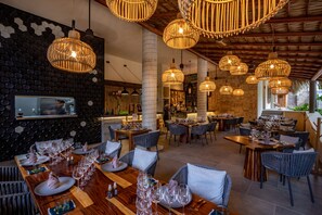 A restaurant with multiple dining areas, wicker pendant lighting, and a stone wall with hexagonal patterns. - Casa Bocana Huatulco (Santa María Huatulco)