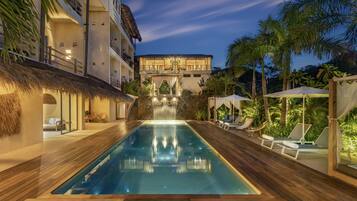 A pool area with a waterfall, lounge chairs, and a thatched-roof structure.