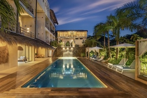 A pool area with a waterfall, lounge chairs, and a thatched-roof structure. - Casa Bocana Huatulco (Santa María Huatulco)