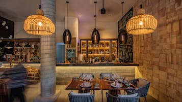 A restaurant with a bar area, wooden tables, and hanging pendant lights.